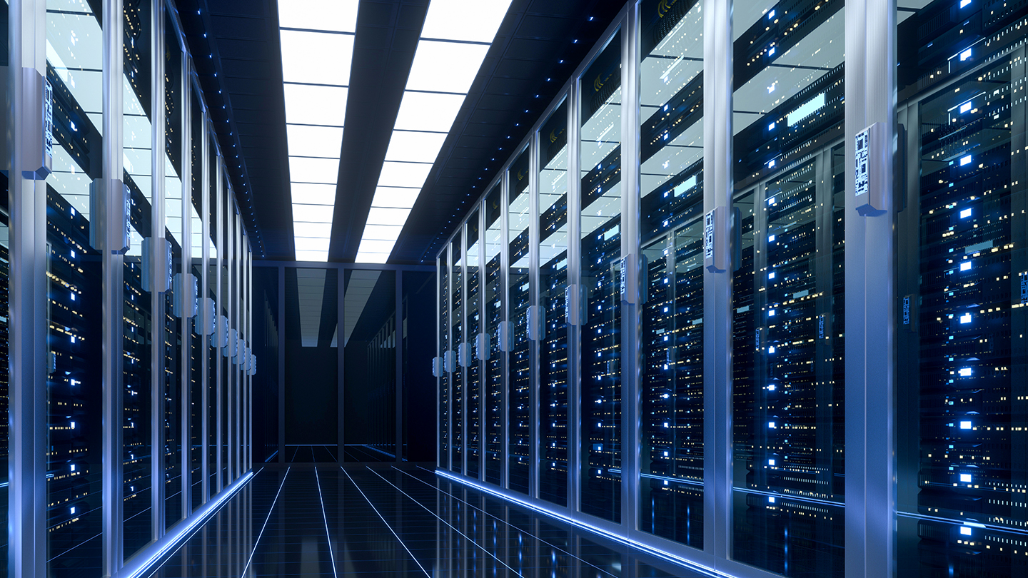 A hallway in a data center with rows of server racks on both sides, illuminated by overhead lights.