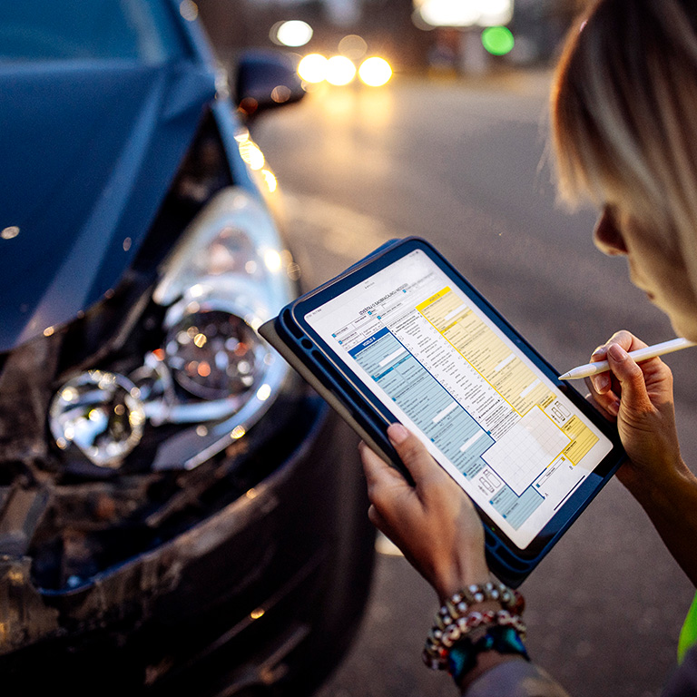 Person filling out an insurance claim form with a car in the background.