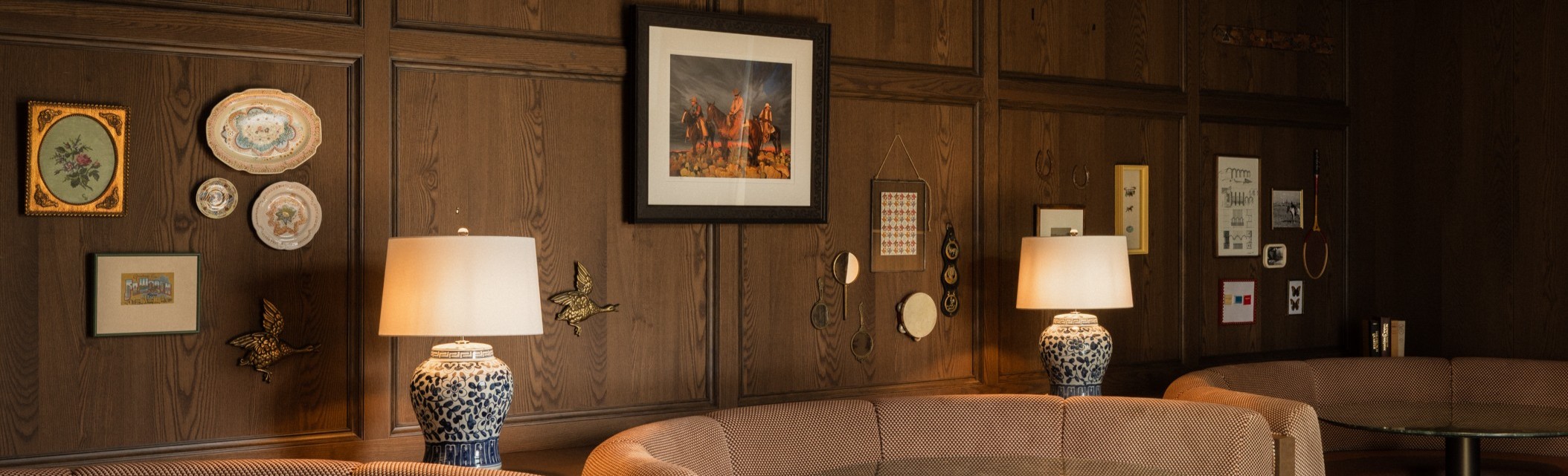 Wood-paneled lounge with curved booth seating, round glass tables, table lamps, and framed art on the wall.