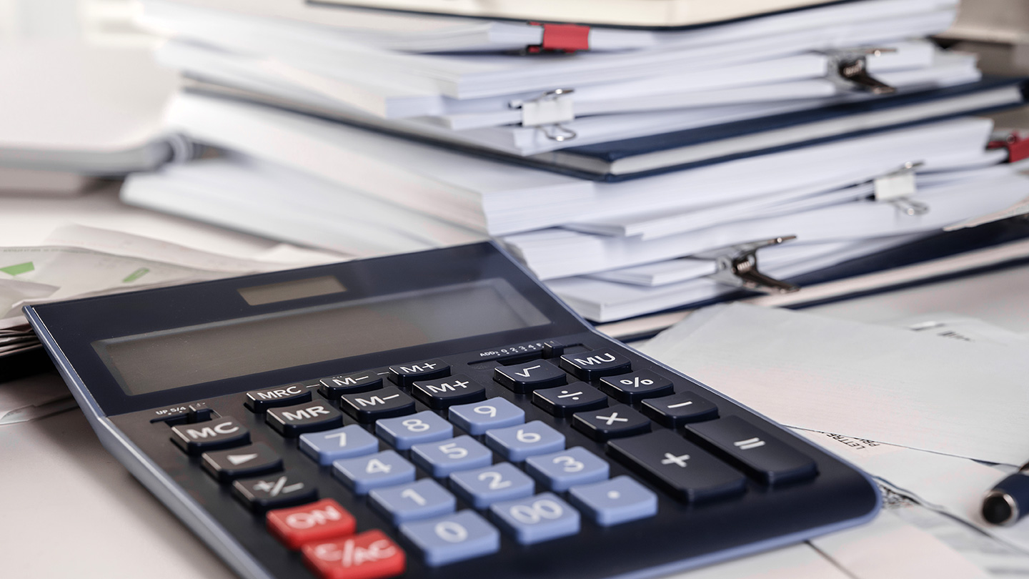 A calculator shown in front of a stack of papers