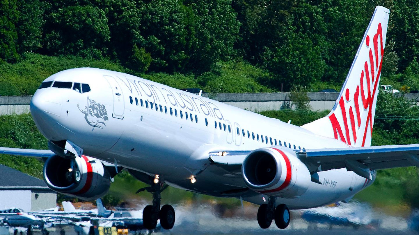 Virgin Australia airplane taking off with green trees in the background.