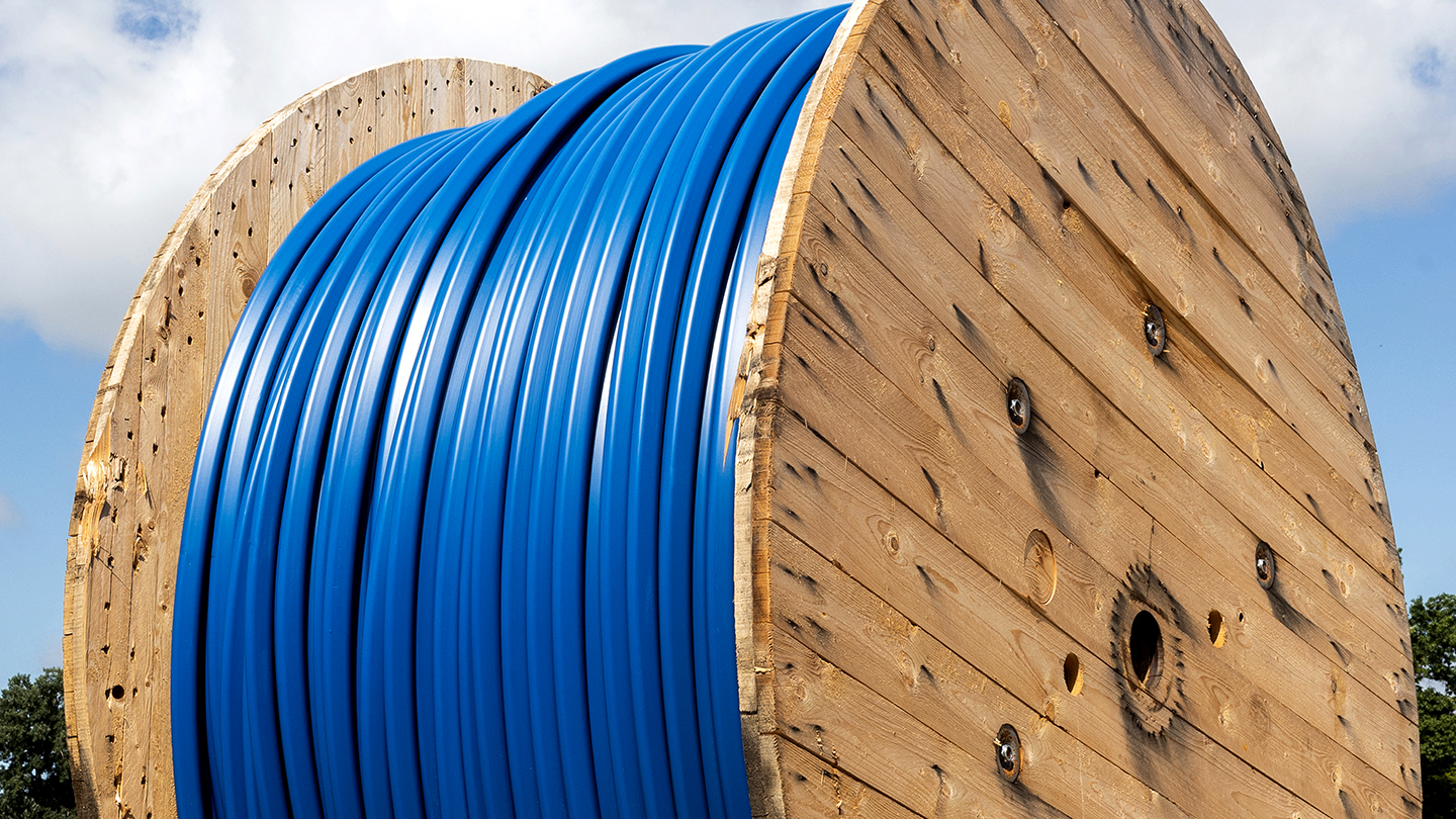 Large wooden spool with blue cable coiled around it, set against a cloudy sky.
